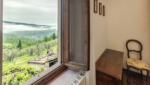A room with a large window overlooking a lush landscape, a wooden chair, and a small table. - Agriturismo Poggio di Montepescoli - L'aia (Pelago)