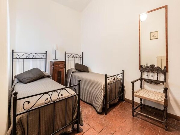A bedroom with two single beds, a wooden nightstand, a chair, and a large mirror on the wall.