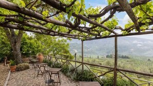 A rustic outdoor seating area with stone flooring and metal furniture, overlooking a lush landscape. - Agriturismo Poggio di Montepescoli - L'aia (Pelago)