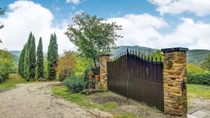 A gravel driveway leading to a black metal gate with stone pillars, surrounded by greenery and trees. - Your Home in a Tuscan Tower (Monterchi)