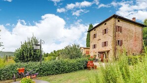 A stone building with a garden in front, a round table with a potted plant, and a street lamp. - Your Home in a Tuscan Tower (Monterchi)