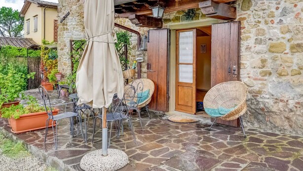 A stone building with a wooden door, outdoor seating with metal chairs and a table, and a hanging umbrella. - Your Home in a Tuscan Tower (Monterchi)