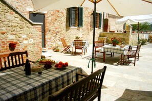 Une terrasse extérieure avec des murs en pierre, des meubles en bois et une nappe à carreaux.