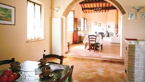 Un comedor con una mesa preparada para dos, una cocina al fondo y una chimenea de ladrillo.