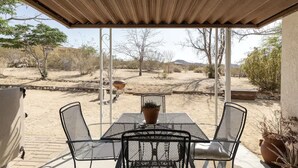 Patio esterno con tavolo e sedie, zona riparata e vista su un paesaggio desertico.