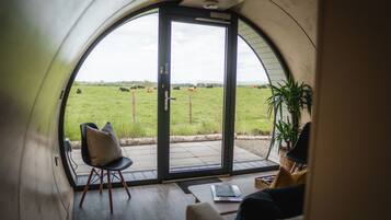 A cozy interior with a large arched window offering a view of a green field with cows.