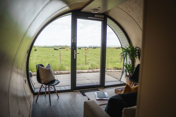 Un interior acogedor con un gran ventanal arqueado que ofrece vistas a un campo verde con vacas.