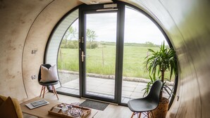 Un interior acogedor con una pared curva, un acceso corredizo a un espacio exterior, un sofá, una mesa con una bandeja y una silla.