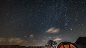 Cielo estrellado con una estructura en forma de cúpula iluminada desde el interior, rodeada de un paisaje cubierto de hierba.