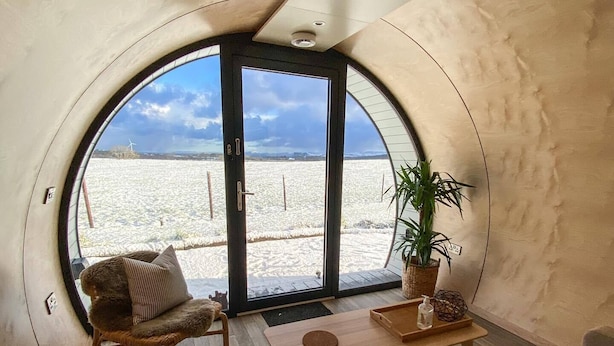 Un interior acogedor con un ventanal redondo, un sillón de mimbre, una mesita y una planta en maceta.