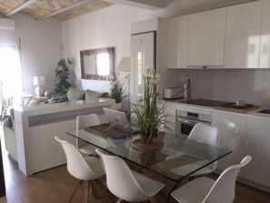 A modern kitchen with white cabinets, a central island with seating, and a dining area with a glass table and white chairs.