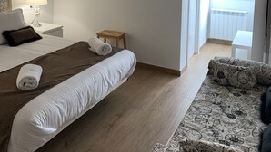 Una camera da letto con un letto, un comodino con una lampada, uno specchio, uno sgabello di legno e vista sul balcone.
