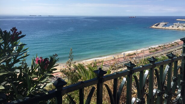 Vista sulla costa con spiaggia, un porto turistico e una nave in lontananza.
