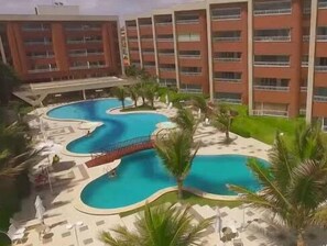 A hotel with a large pool area, palm trees, and a red bridge. - Scopa Beach Resort Apartments (Aquiraz)