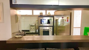 A kitchen with a microwave, coffee maker, and refrigerator. There are wicker chairs in front of the counter. - Scopa Beach Resort Apartments (Aquiraz)