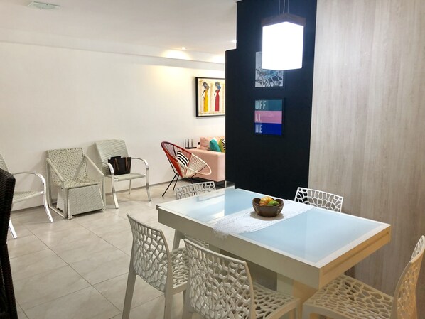 A modern dining area with a white table, white chairs, and a black accent wall with artwork.