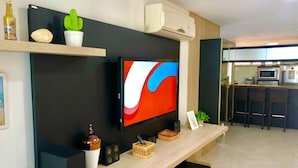 A modern living room with a flat-screen TV, a coffee table, and a kitchen area in the background. - Scopa Beach Resort Apartments (Aquiraz)