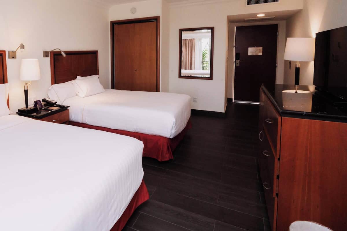 A hotel room with two beds, wooden headboards, a nightstand with a lamp, a mirror, and a dresser.