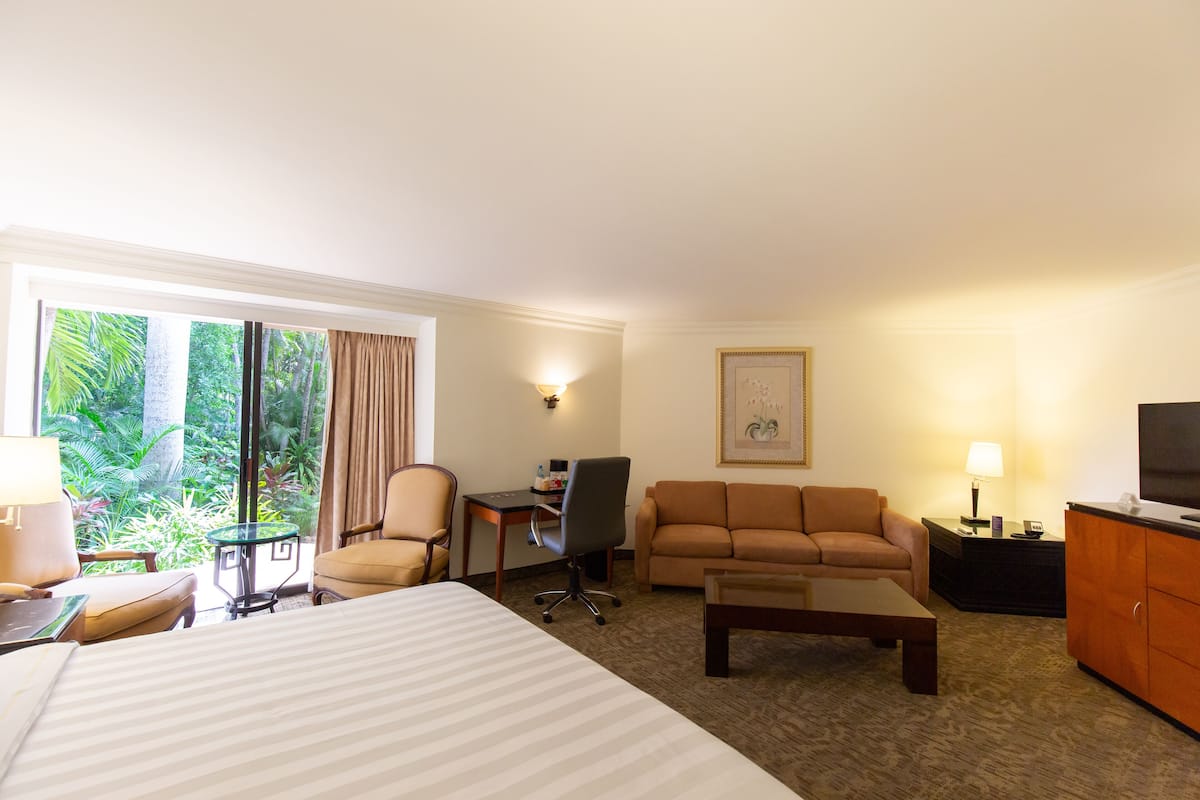 Habitación de hotel con cama, sofá, escritorio, silla, televisor y vistas al exterior.