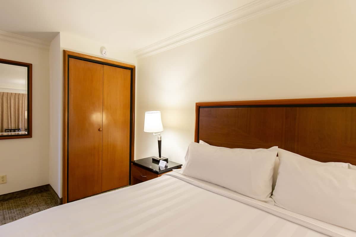 A hotel room with a large bed, a wooden headboard, a nightstand with a lamp, and a wooden wardrobe.