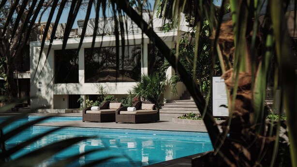 Zona de piscina con un moderno espacio de descanso y un edificio con grandes ventanales al fondo.