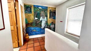 Un couloir orné d’une fresque murale, une porte en bois, une fenêtre avec des stores et un sol carrelé.