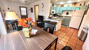 Un coin repas avec une table en bois, des chaises, un vase de fleurs, une lampe et un téléviseur.