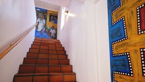 Un escalier muni d’une rampe, menant à une pièce dont le mur est orné d’une fresque colorée.