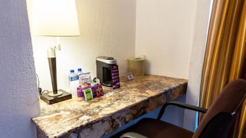 Escritorio de habitación de hotel con lámpara, caja de pañuelos, botella de jabón para manos y un pequeño cubo de basura.