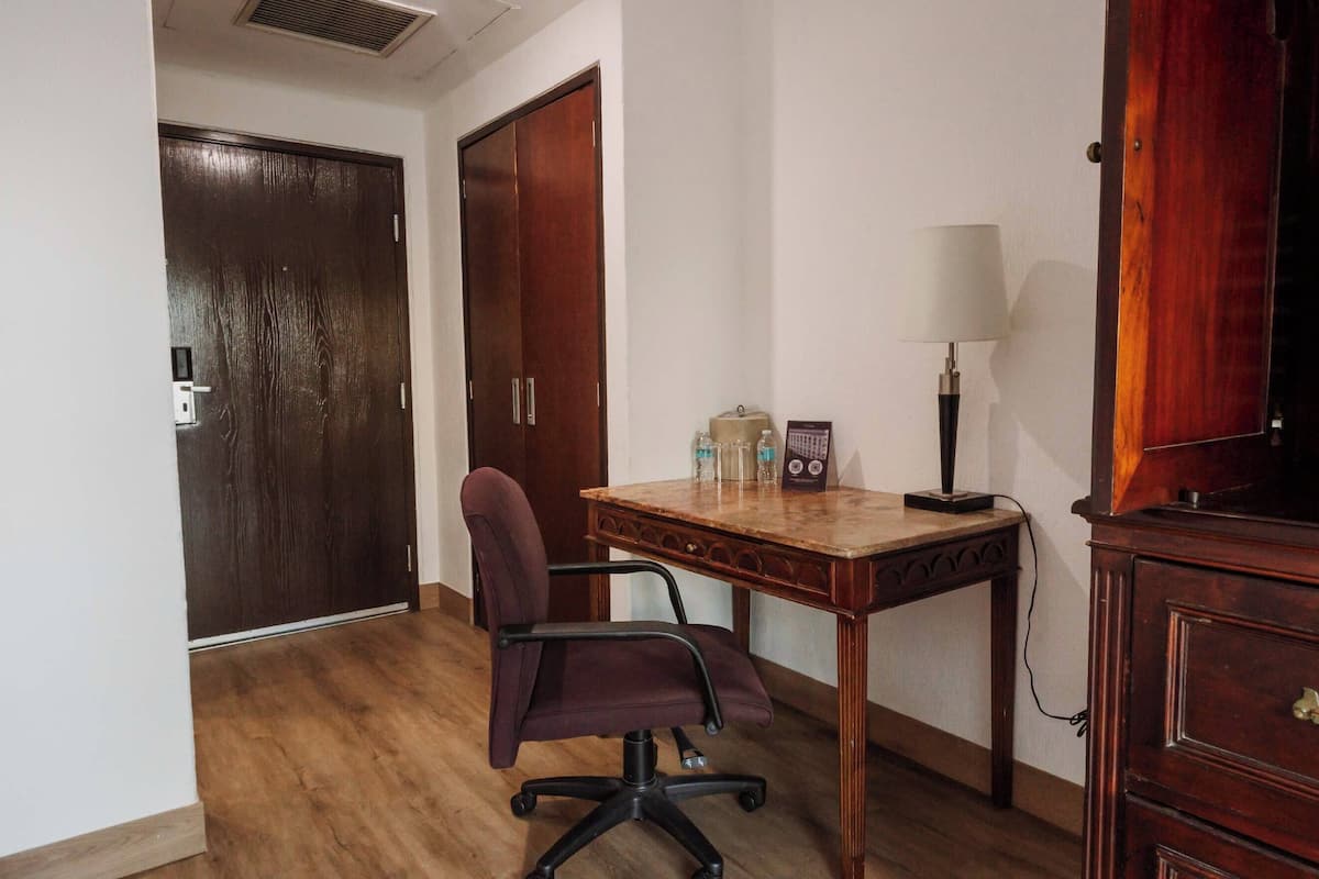 A room with a wooden desk, a chair, a lamp, a television, and a wardrobe.
