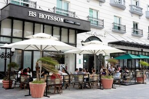 An outdoor cafe area with tables and umbrellas, a hotel sign, and a building facade with balconies. - HS HOTSSON Smart Value Tampico (Tampico)