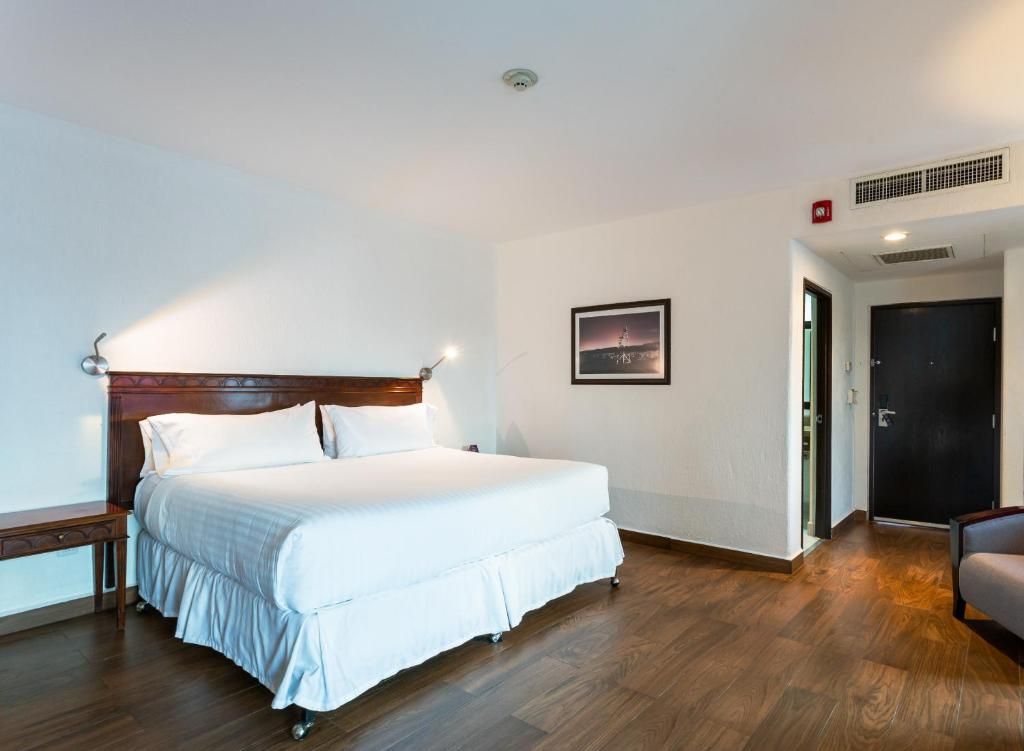 A hotel room with a large bed, a bedside table, a chair, a door, and a picture on the wall.