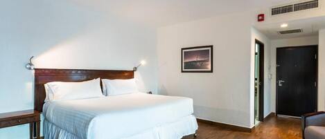 A hotel room with a large bed, a bedside table, a chair, a door, and a picture on the wall.