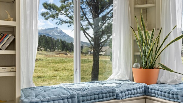 Una habitación con asiento junto a la ventana, estantería, planta en maceta y vistas a un paisaje montañoso.