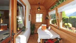 Une cabane en bois avec une table et des chaises, une fenêtre donnant sur les montagnes et une porte avec un cadre en bois.