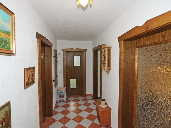 A hallway with a checkered floor, wooden doors, and a small stool.