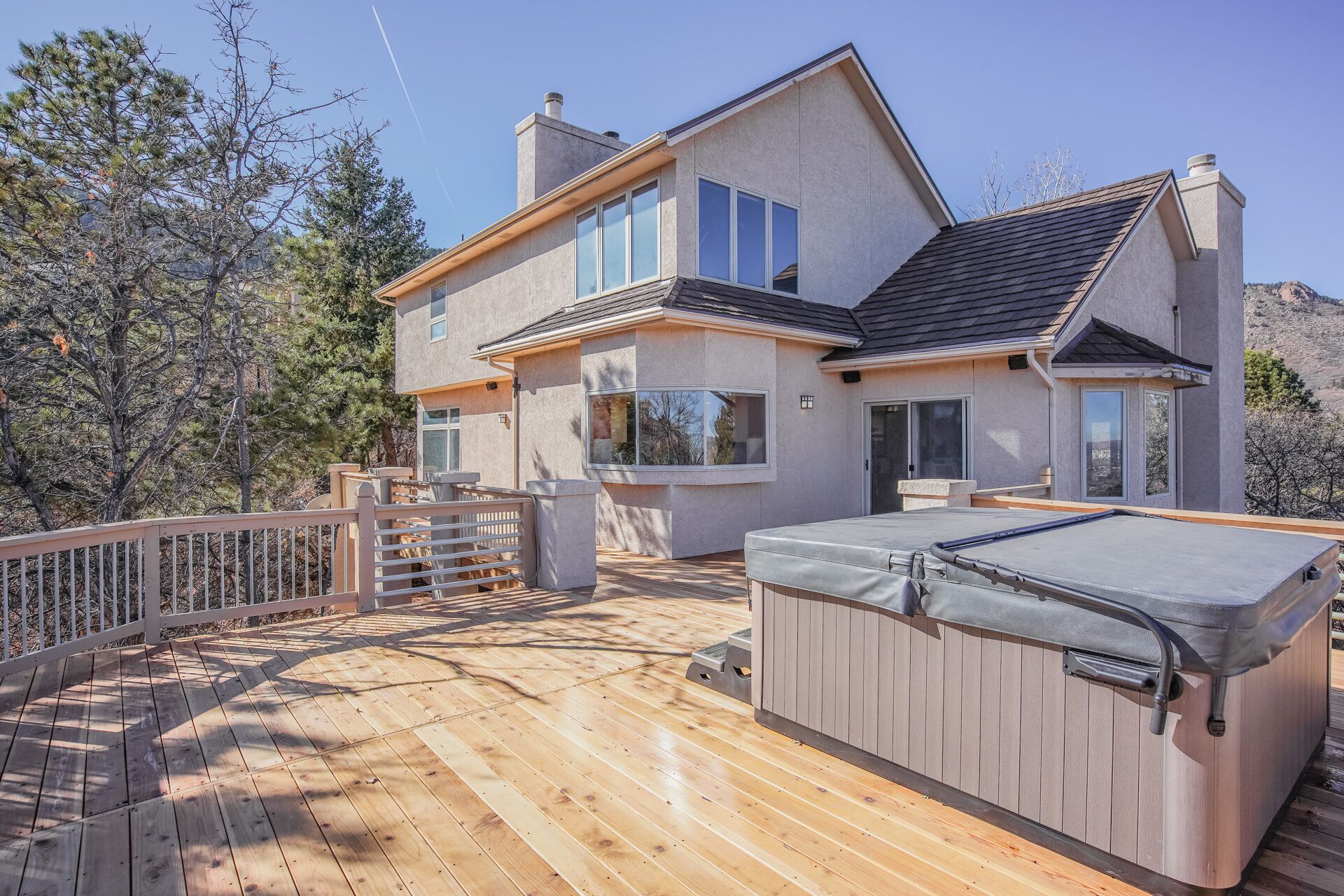 A modern two-story house with a wooden deck, a hot tub, and a view of the surrounding landscape.