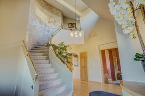 A spiral staircase with a handrail, a plant on the landing, and a door in the background.