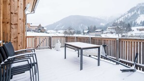A wooden deck with a table and chairs, overlooking a snowy village and mountains. - Chalet in Hohentauern With Sauna Near ski Area (Hohentauern)