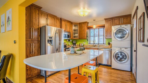 A modern kitchen with wooden cabinets, stainless steel appliances, a central island with stools, and a washing machine. - Stir Crazy! Bike Trails, Dogs OK, Food & Nightlife (Colorado Springs)