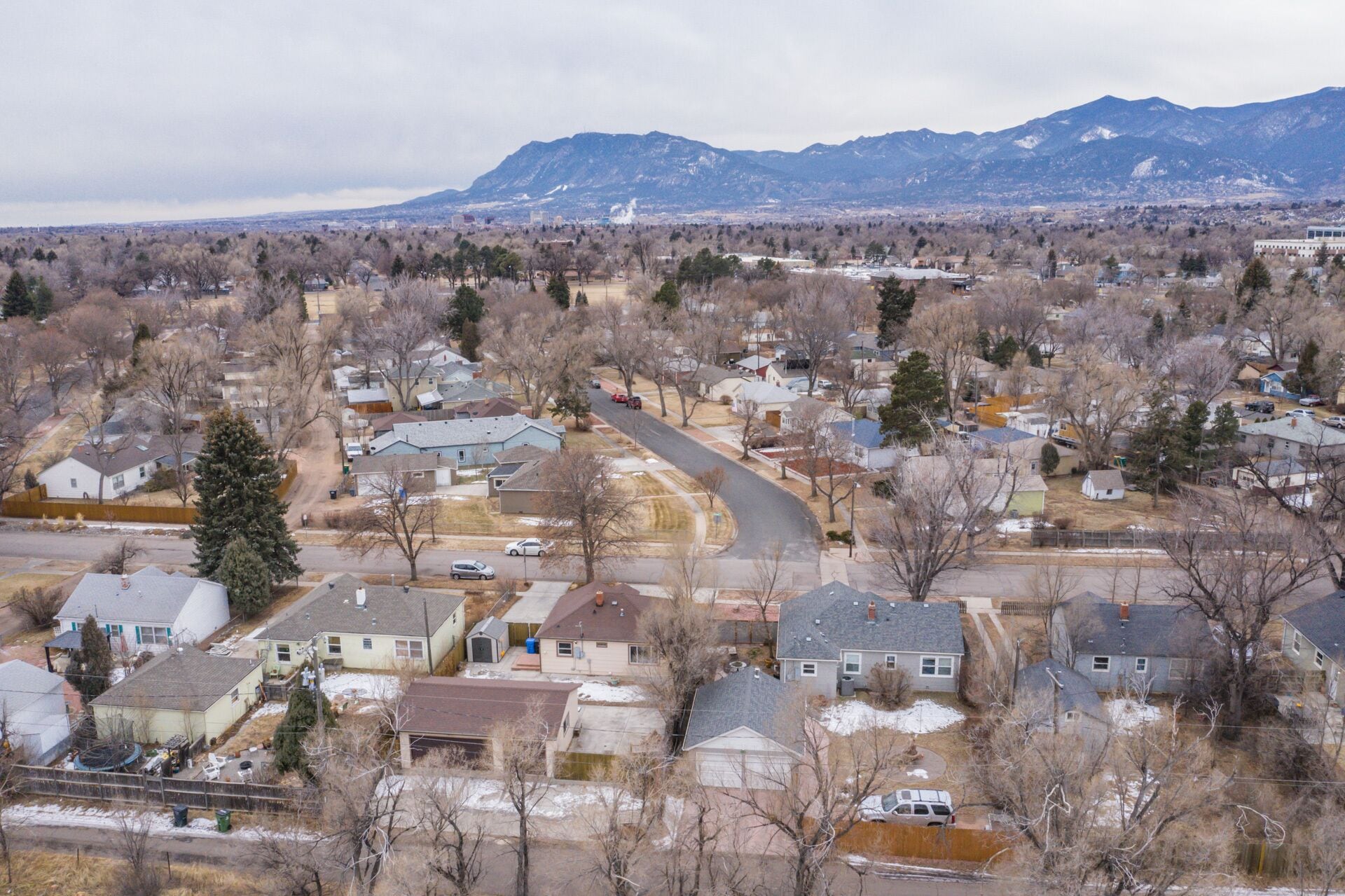 A residential area with houses, a winding road, and mountains in the background.