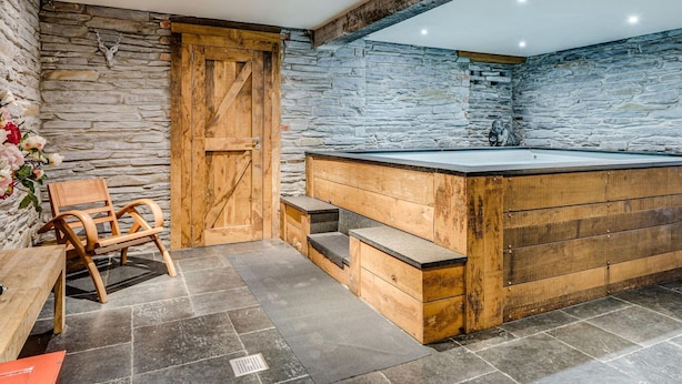 Un baño rústico con pared de piedra, bañera de madera y un banco de madera.