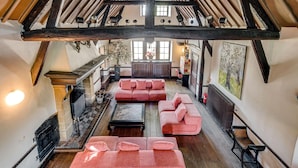 Amplio espacio tipo loft con vigas de madera a la vista, un piano y una zona de estar acogedora con sofás rosados.