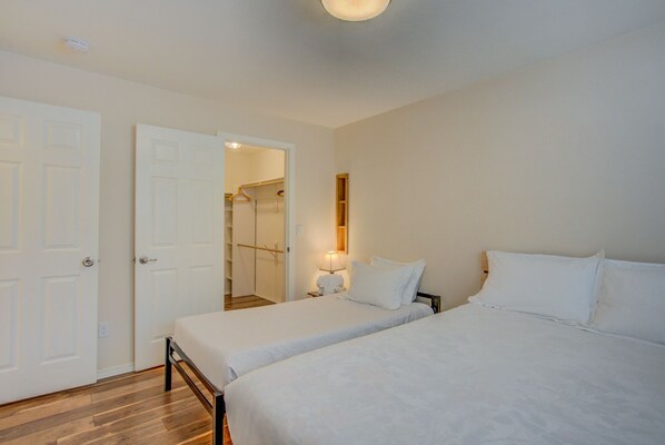 A bedroom with two single beds, a wooden floor, a white door, and a closet with a mirror and a hanging rack.
