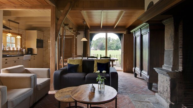 A cozy interior with a wooden ceiling, a dining area with a table and chairs, and a view of a green landscape through a large window. - Farmhouse in Enschede Near Forest (Enschede)