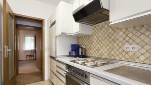 Une cuisine compacte équipée d’une cuisinière à gaz, d’un four et d’un four à micro-ondes. On y trouve une machine à café sur le plan de travail, et le pare-feu présente un motif géométrique.