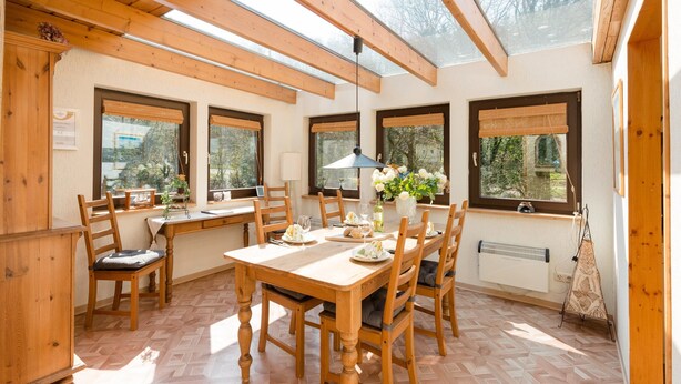 A dining area with a wooden table and chairs, large windows, and a skylight. - Eichenborn Gartenaufenthalt (Bad Pyrmont)