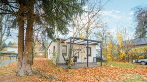A small house with a covered porch, surrounded by trees and fallen leaves. - Gartenbungalow in Blankenfelde-mahlow (Blankenfelde-Mahlow)