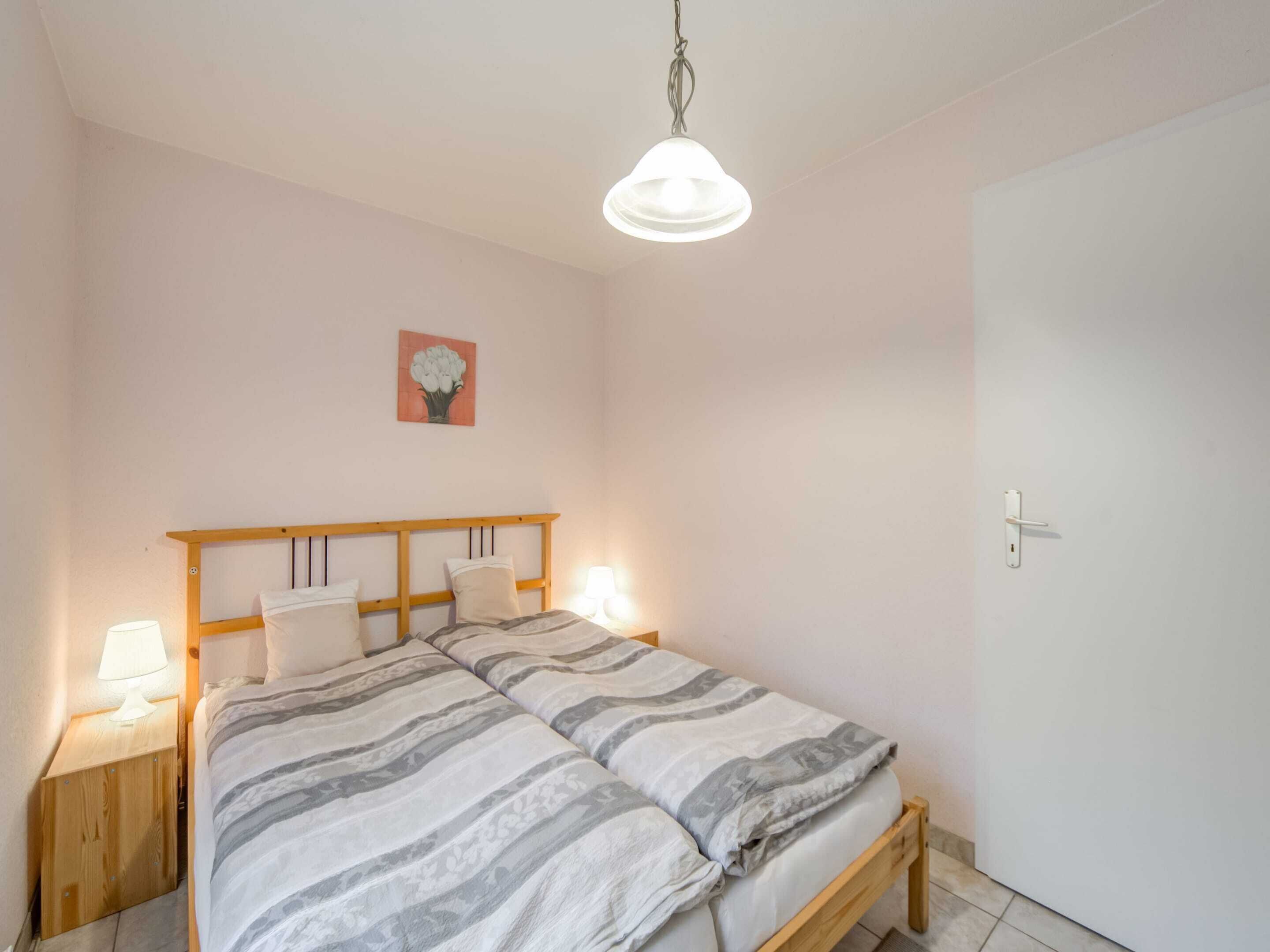 Une chambre à coucher avec un lit en bois, deux tables de chevet avec des lampes, un luminaire fixé au mur et une porte.