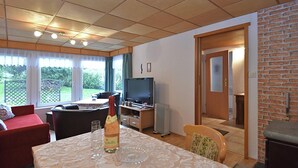 Uma sala de estar acolhedora com televisão, uma mesa de jantar com uma garrafa de vinho e uma lareira.